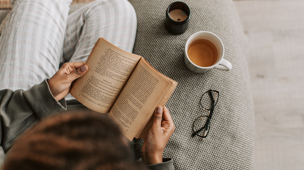 Person reading a book on a couch, with a cup of tea and glasses nearby. The scene conveys a cozy and relaxed atmosphere.