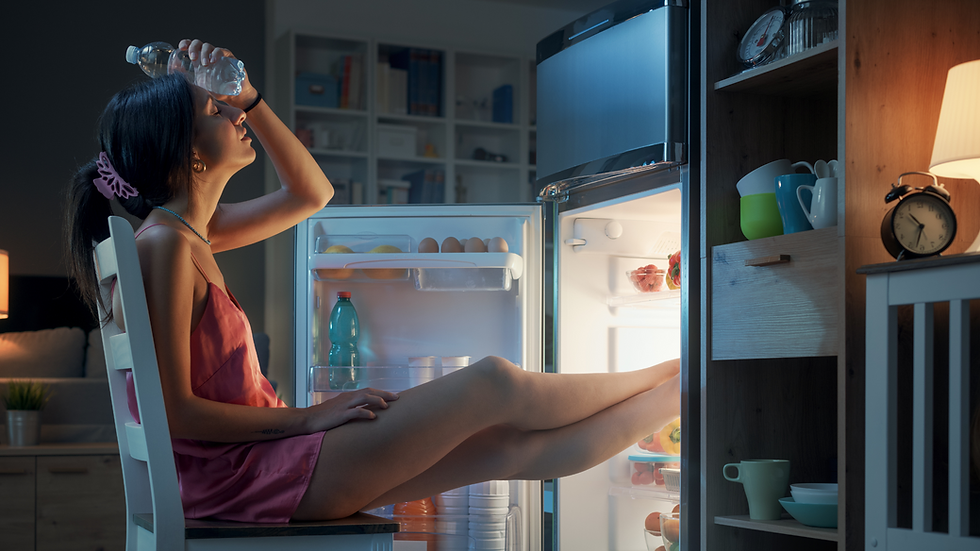 Woman sitting in front of an open refrigerator trying to cool down, representing excess heat and Pitta dosha imbalance.