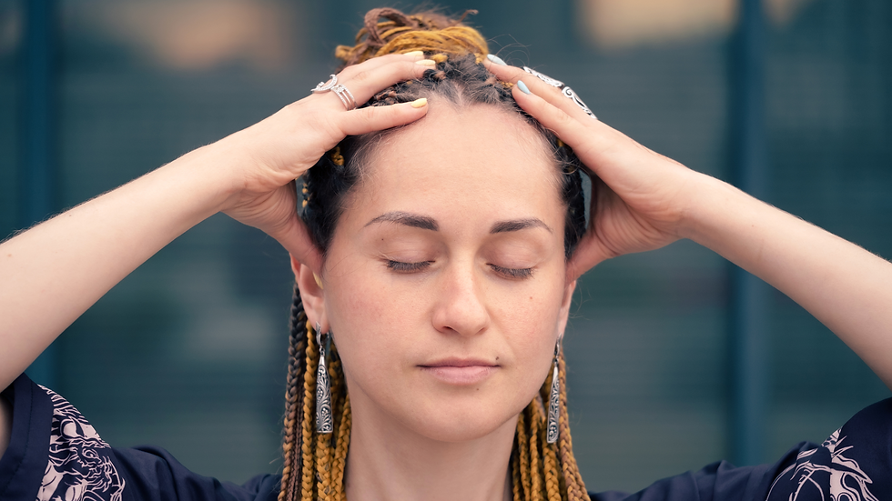 Close-up of a woman with braided hair and rings, eyes closed, hands on her head in a calm, meditative pose.