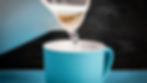 A kettle pours steaming water into a blue mug. The background is dark wood, emphasizing the contrast with the bright mug.