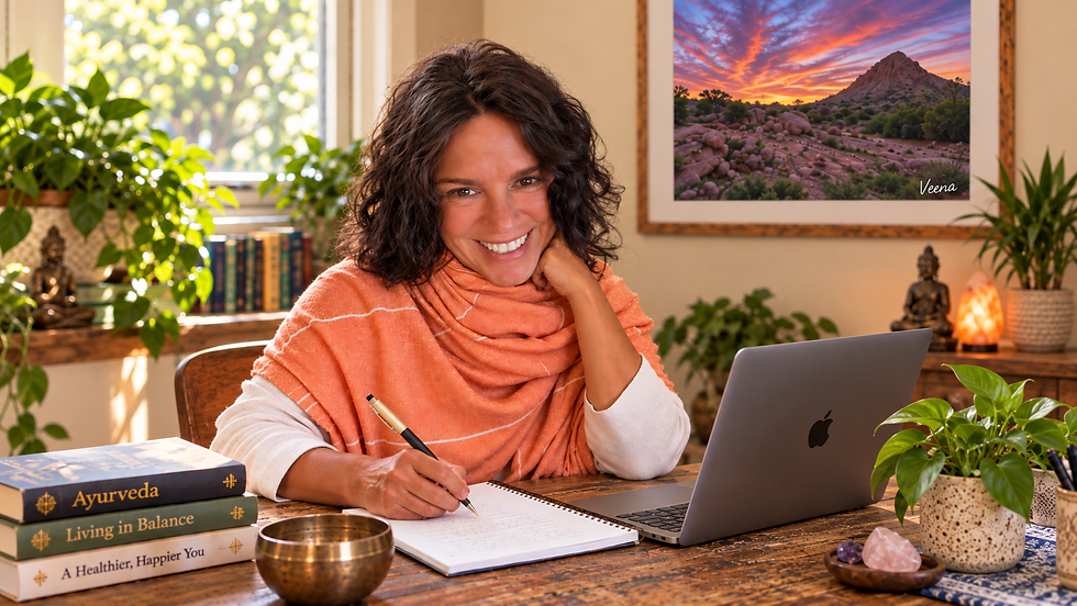 Smiling Veena in an orange shawl writes in a notebook beside a laptop in a cozy plant-filled office, with Ayurveda books nearby.