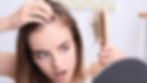 Woman looks worried while examining hair loss on a brush. She parts her hair, showing concern. Zigzag pattern in the background.