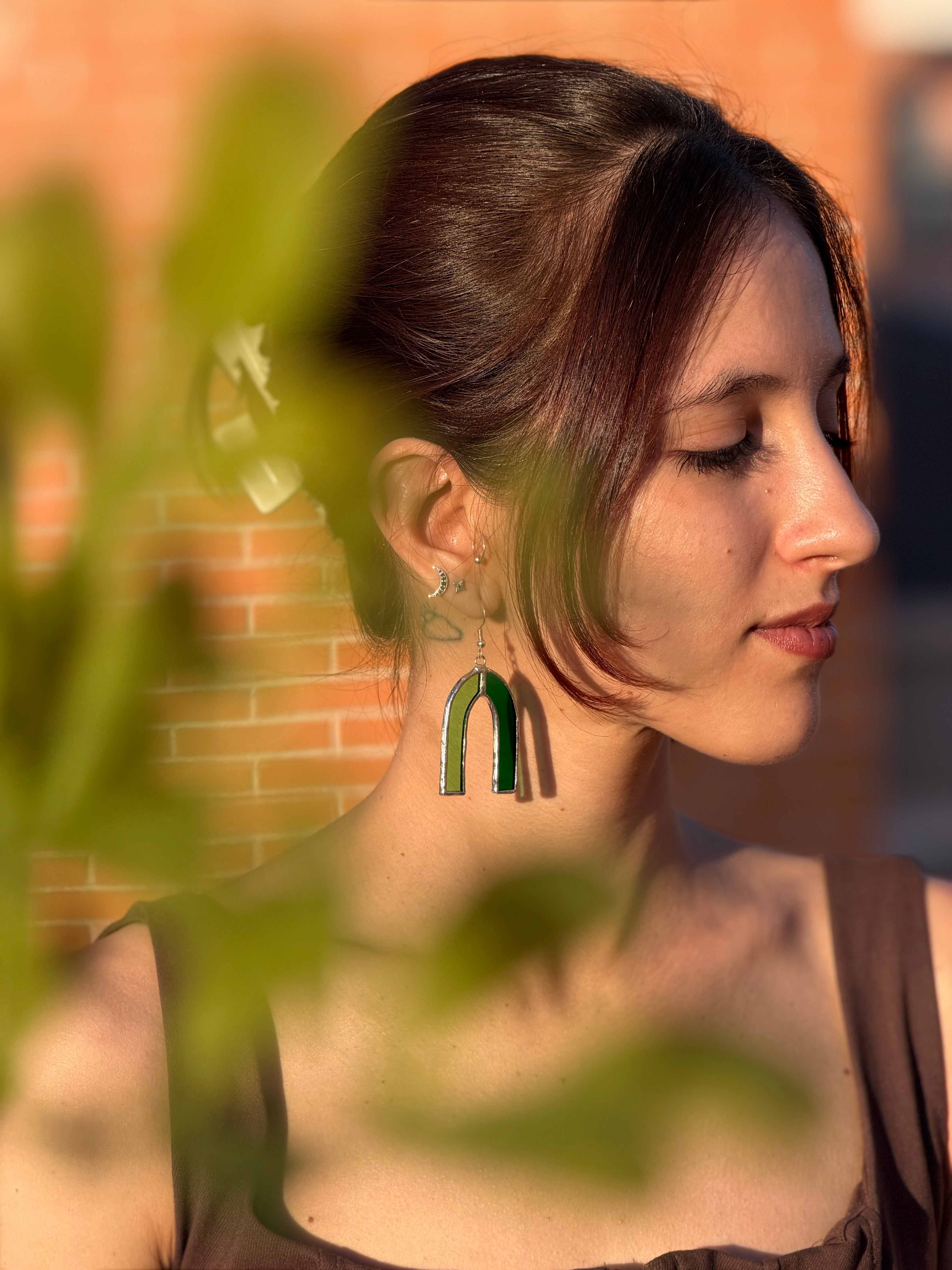 Chica de perfil posando con pendientes de vidrio bicolor verde claro y verde oscuro en forma de herradura y con gancho de pla