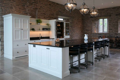 a bespoke, handmade shaker kitchen fitted into a grand country home with the kitchen cabinetry painted in a soft white colour paired with luxurious stained oak interior and a dramatic black worktop