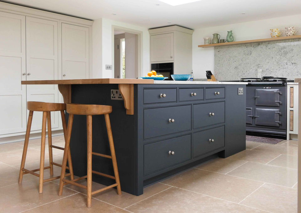 a handcrafted bespoke shaker kitchen with soft grey kitchen cabinetry and a dark blue kitchen island with a bespoke oak worktop. This kitchen design features a stunning shaker countertop, integrated appliances, a tall oak larder, innovative storage solutions, bespoke kitchen cabinetry and a shaker-inspired utility room with soft grey cabinetry and satin nickel handles.
