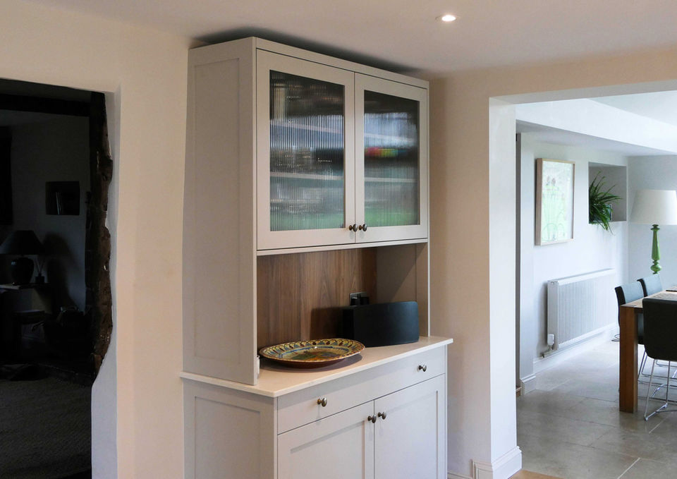 A handmade, modern kitchen with light grey kitchen cabinetry and a luxurious walnut island. This kitchen design features innovative storage solutions, walnut spice racks, bespoke walnut shelving, glazed cabinetry and handmade bespoke kitchen features
