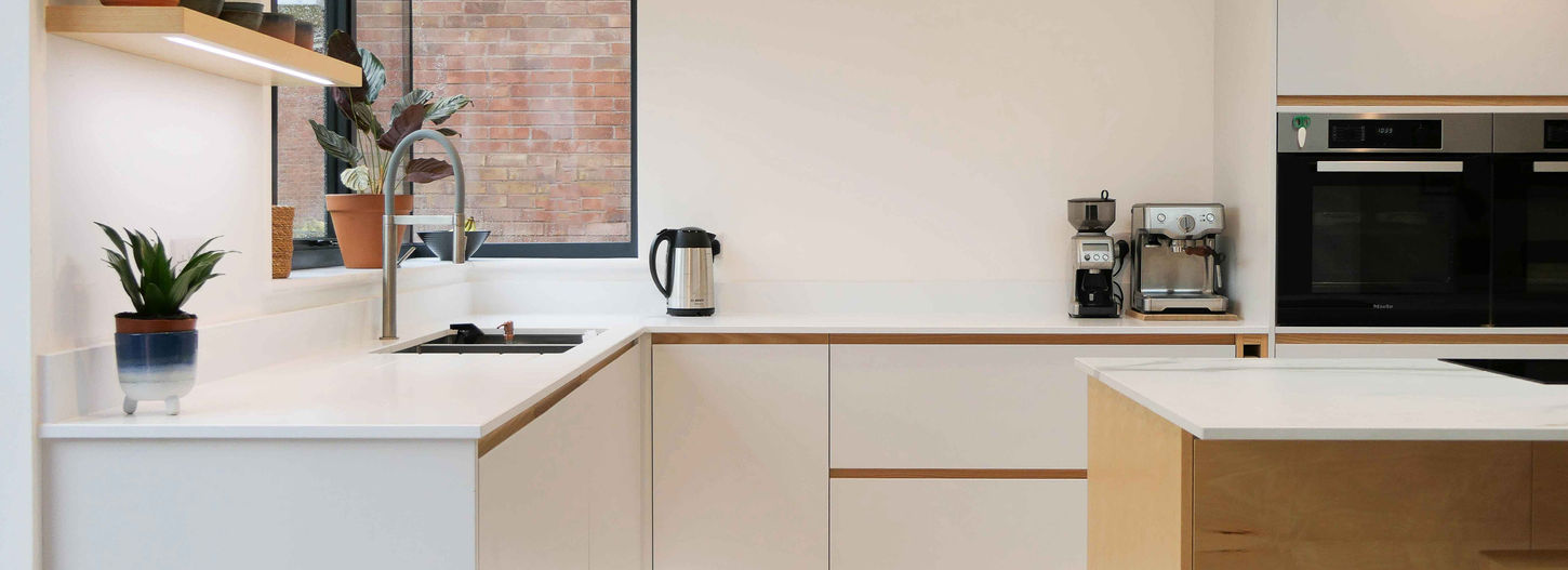 a handcrafted bespoke modern kitchen with pristine white cbainetry, oak wooden detailing, an innovative hidden handle design and bespoke kitchen detailing