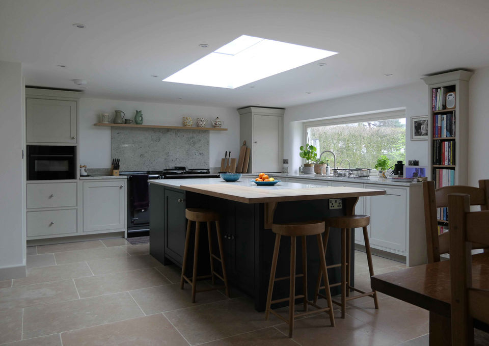a handcrafted bespoke shaker kitchen with soft grey kitchen cabinetry and a dark blue kitchen island with a bespoke oak worktop. This kitchen design features a stunning shaker countertop, integrated appliances, a tall oak larder, innovative storage solutions, bespoke kitchen cabinetry and a shaker-inspired utility room with soft grey cabinetry and satin nickel handles.