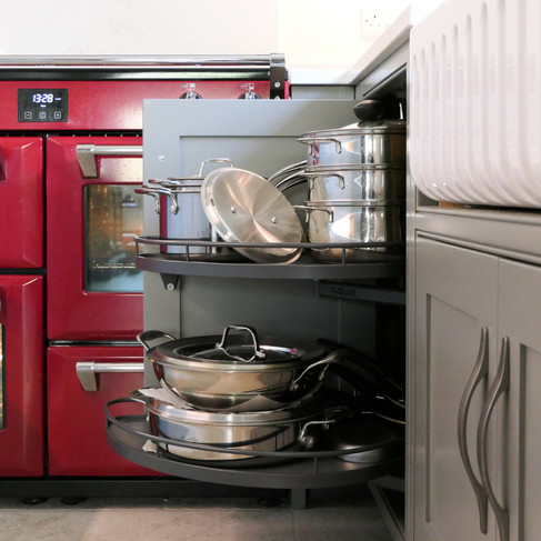 a handcrafted bespoke shaker kitchen painted in a soft grey colour featuring an innovative corner storage system with two kidney-shaped trays that pull out of the cabinet 