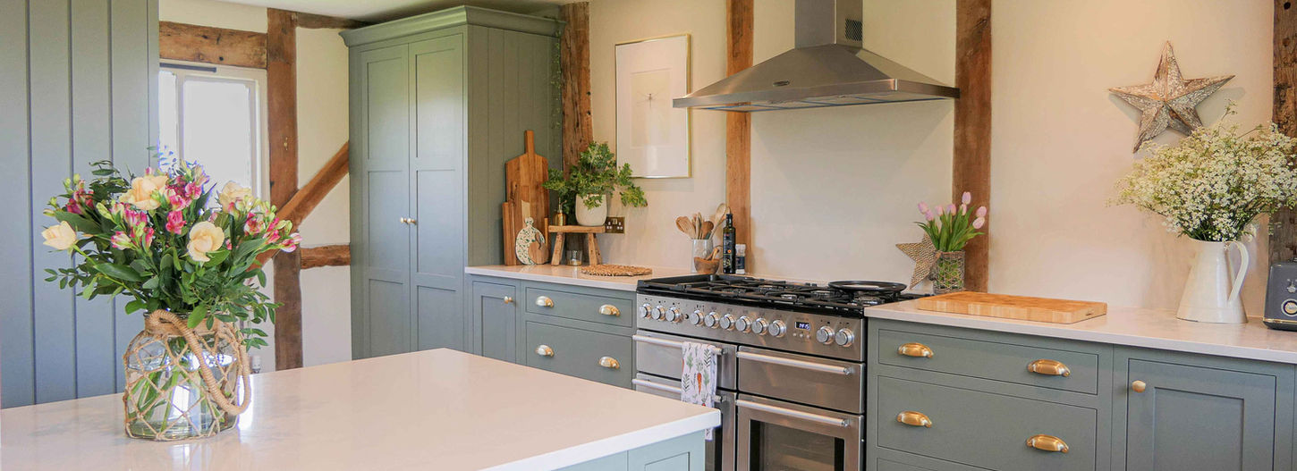 a handcrafted bespoke shaker kitchen painted in a soft green colour and paired with satin brass handles, featuring bespoke cabinetry detailing