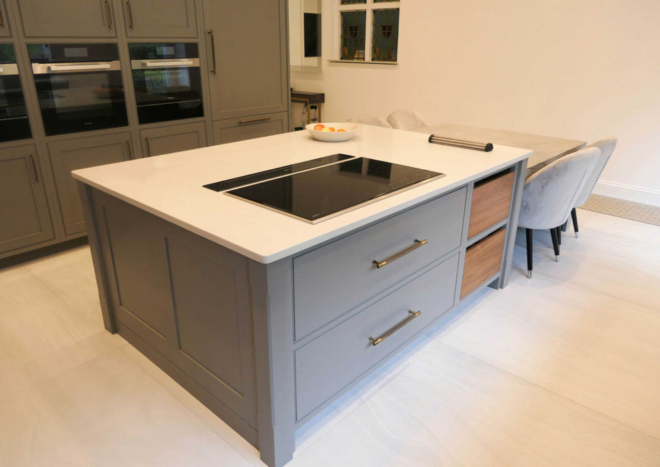 a beautifully handcrafted, bespoke shaker kitchen with smoky grey kitchen cabinetry, luxurious walnut wood features, aged brass handles, integrated state-of-the-art appliances, and bespoke kitchen details