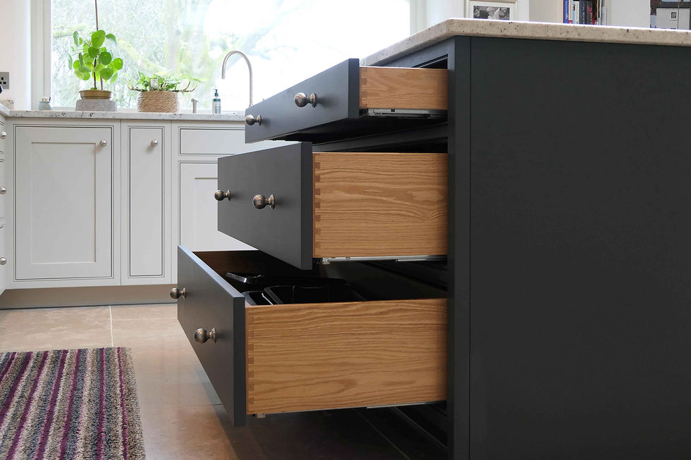 a handcrafted, bespoke shaker kitchen painted in a soft grey colour featuring a dark grey kitchen island with several oak drawers open showcasing the visible dovetail joints on the drawers