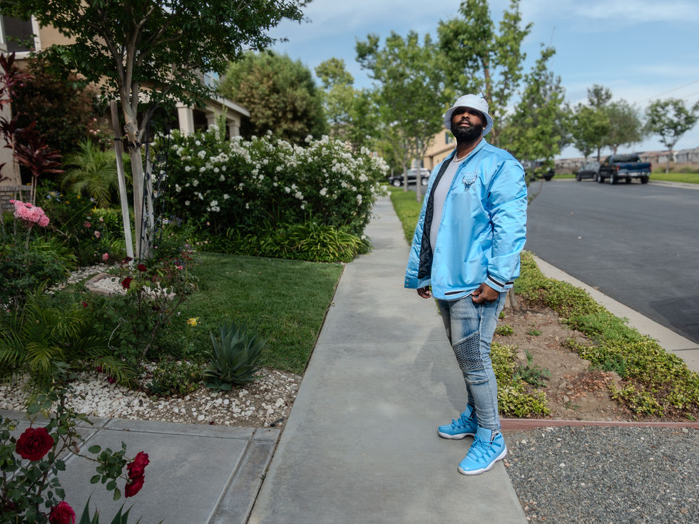 a man wearing a light blue jacket and a white hat stands on a sidewalk