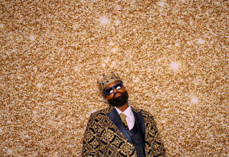 a man wearing a crown and sunglasses sits in front of a gold background