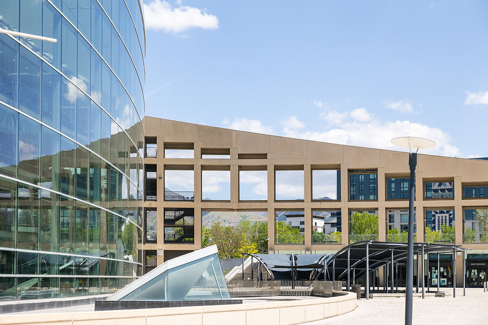 Modern urban scene with glass and concrete buildings under a blue sky. Reflections on windows and a streetlamp in the foreground.