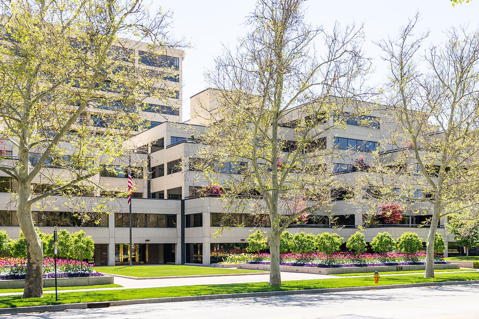 Modern office building with trees and colorful flowerbeds in front. American flag on a pole. Bright, sunny day; peaceful setting.