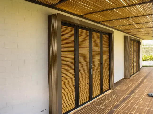 Corredor con pérgola de bambú y puertas artesanales en casa de campo.