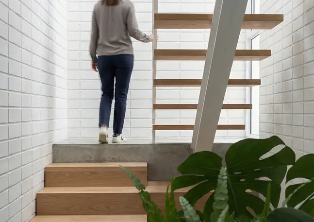 Detalle arquitectónico de escaleras en madera y metal con luz cenital.