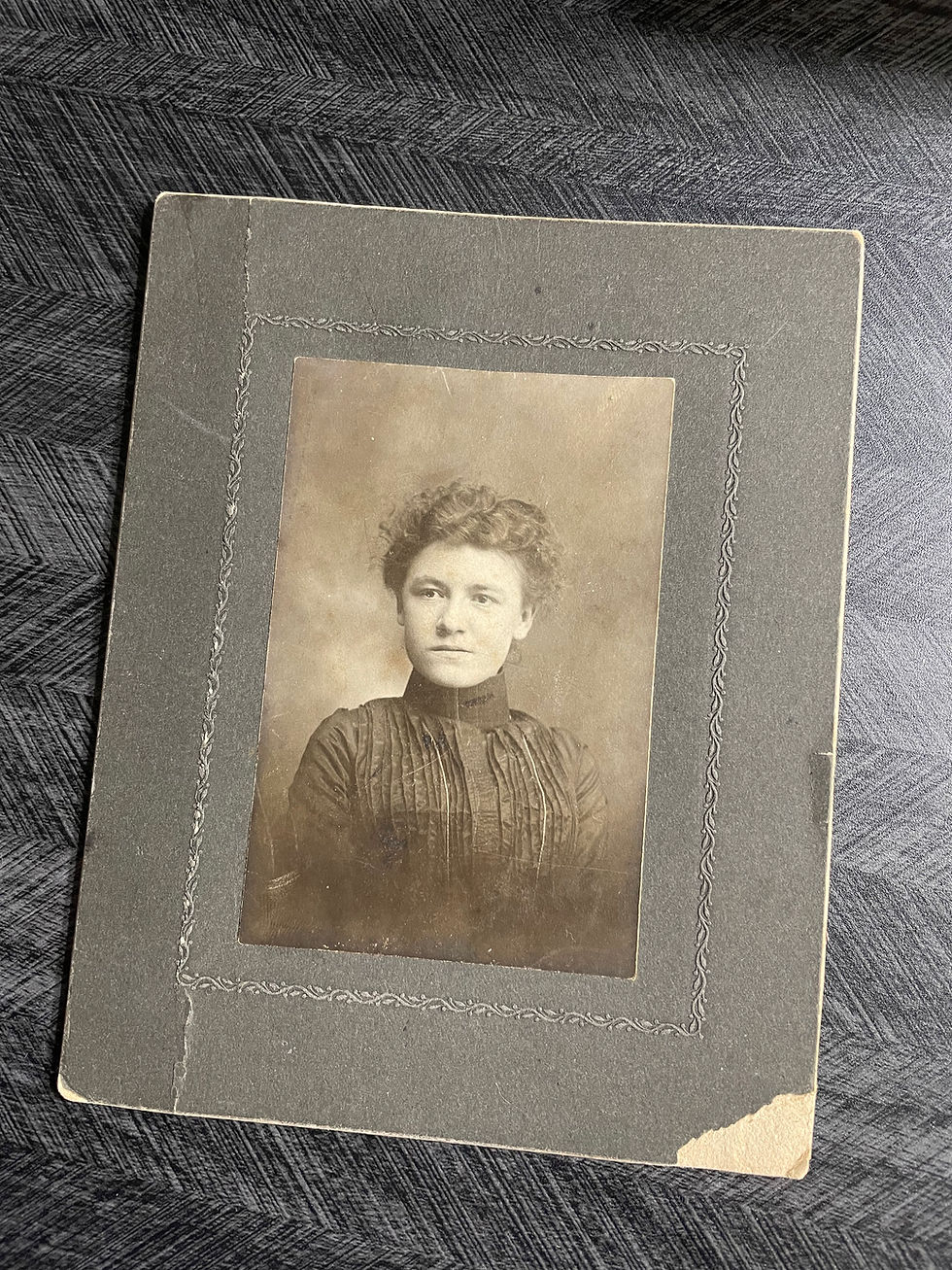 Vintage photo of a woman with curly hair in a dark dress, set against a textured black-and-white backdrop in a worn frame.