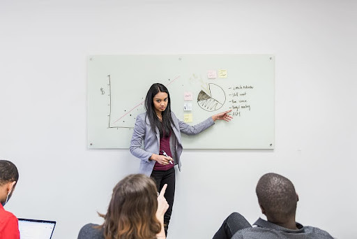 Woman presenting graph on whiteboard to a group of people.