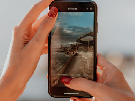 Woman's hands holding a phone, capturing a photo of a the beach, telling a story of her day as it happens.