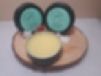 Thumbnail: Two tins and one open black tin with cream on a circular wood cutting with snow flakes and berries