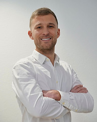 Homme en chemise blanche.
Coupe de cheveux courte.
Sourire ouvert et posture détendue.
Présenté comme Directeur Général.