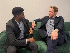 Deux collaborateurs en tenue professionnelle discutant assis sur un canapé dans un espace de bureau.