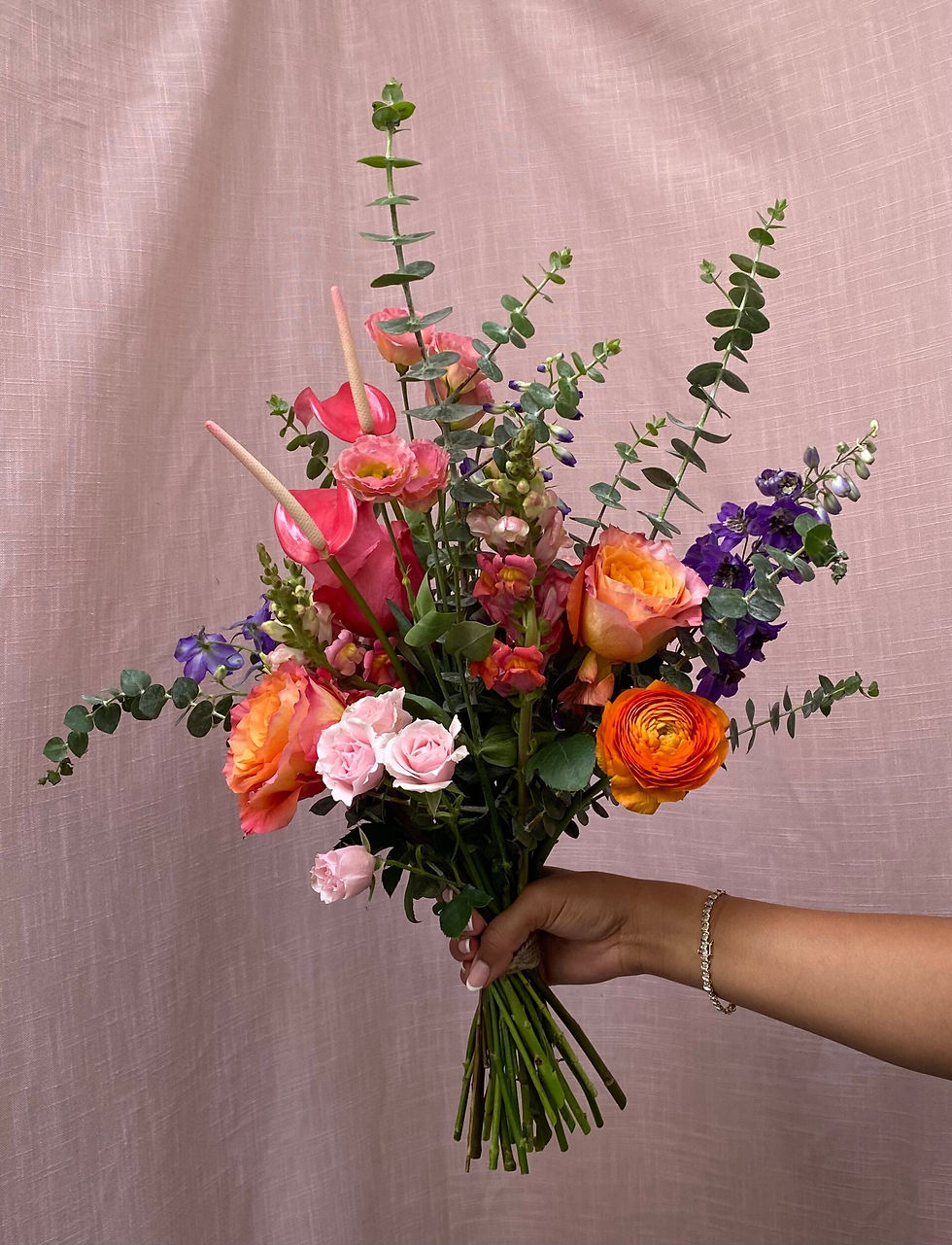 Person holding a vibrant bouquet of flowers with mixed blooms, including roses, lilies, and daisies