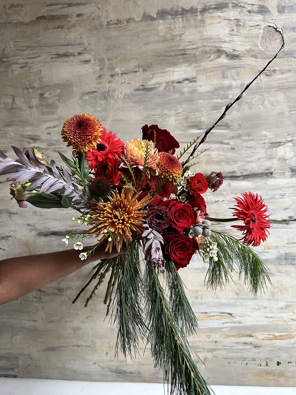 Person holding a vibrant bouquet of flowers with mixed blooms, including roses, lilies, and daisies