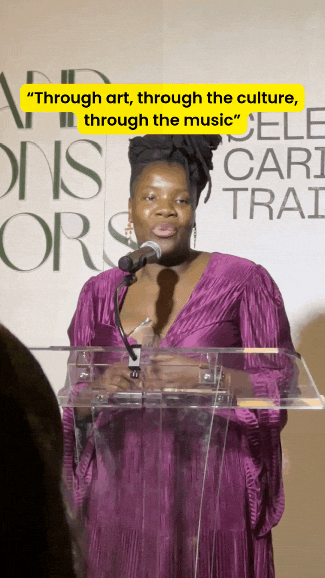 A lady with purple dress speaks passionately about her business behind her a white backdrop with lights
