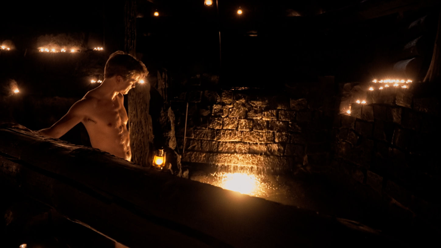 Samuel Aarnio enters a small natural creek within the underground smoke sauna in the Sauna Channel episode: Storfinnhova Gård in Björkboda, Finland.
