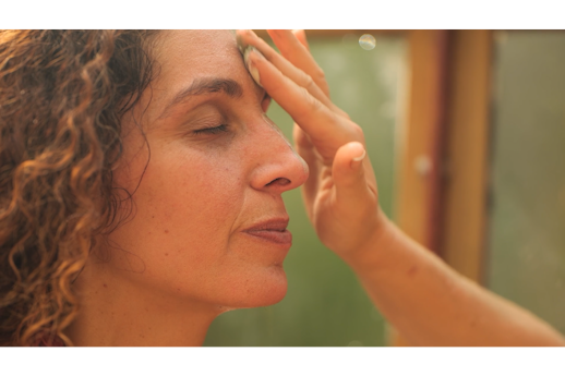 A woman closes her eyes and enjoys the tranquil atmosphere of the Wild Spa Wowo forest steam sauna while a hand applies an herbal therapeutic paste to her forehead on the Wild Spa Wowo episode of Sauna Channel