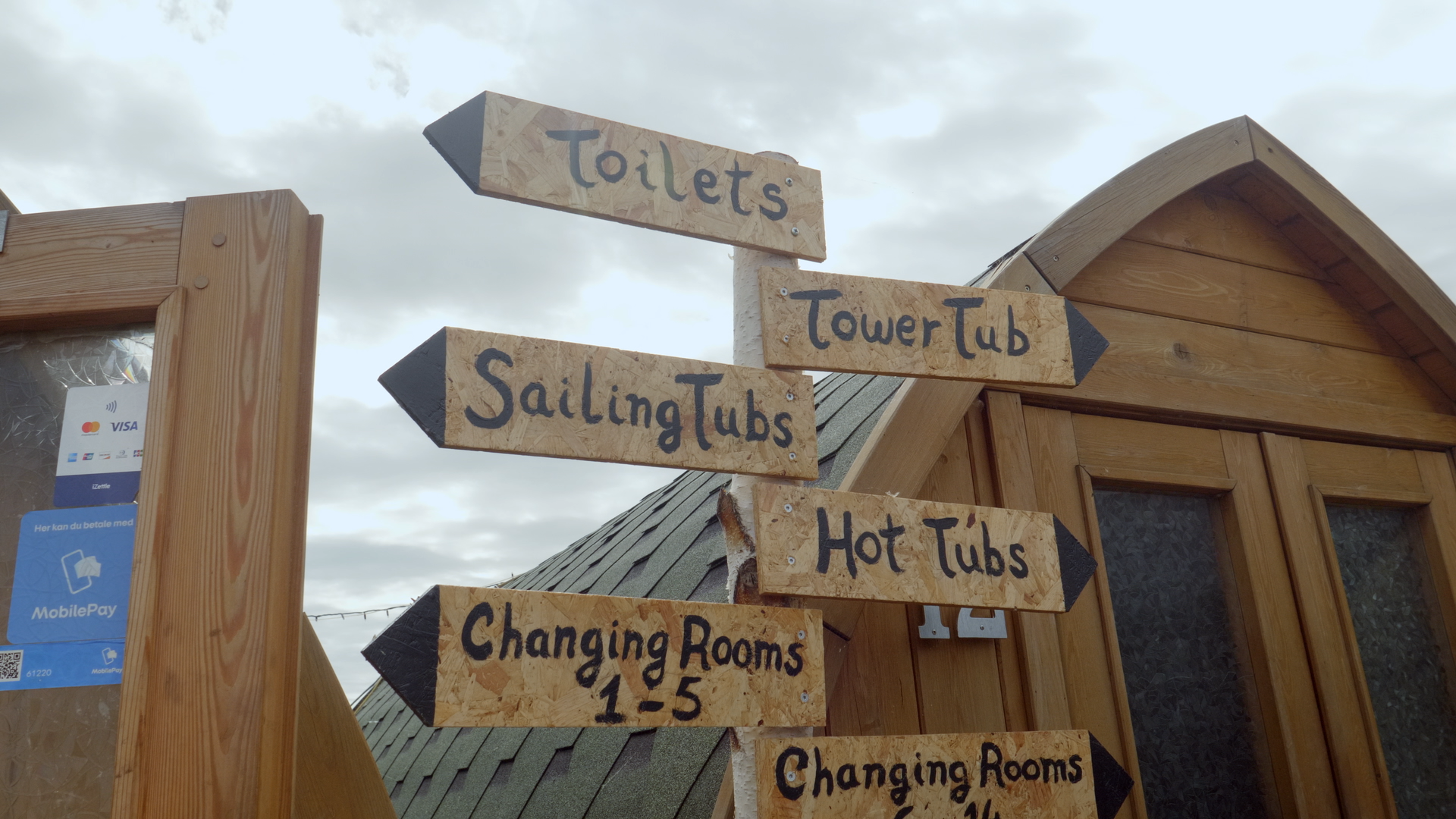 On the CopenHot episode of Sauna Channel in Copenhagen, Denmark, a wooden sign points towards the toilets, the towertub, the sailing tubs, the hot tubs, and the changing rooms 