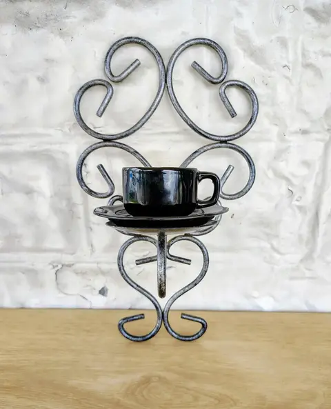 a metal heart frame with a candle holder holding a black teacup on a black plate
