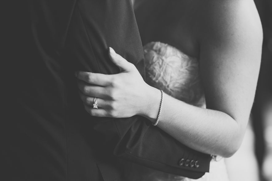 A bride holds hands with a groom with her bracelet and wedding ring in a black and white image.