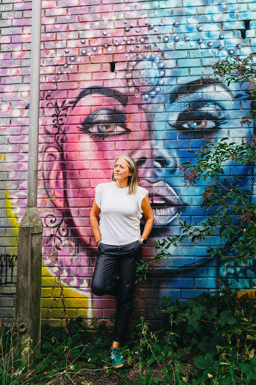 Jo is looking pensive, standing outside against a vibrant mural