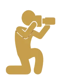Minimalist digital icon of a photographer kneeling while capturing a shot. Gold figure against a solid black background.