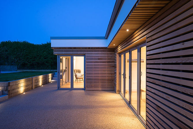 A building, cladded in wood. The rooms are illuminated.