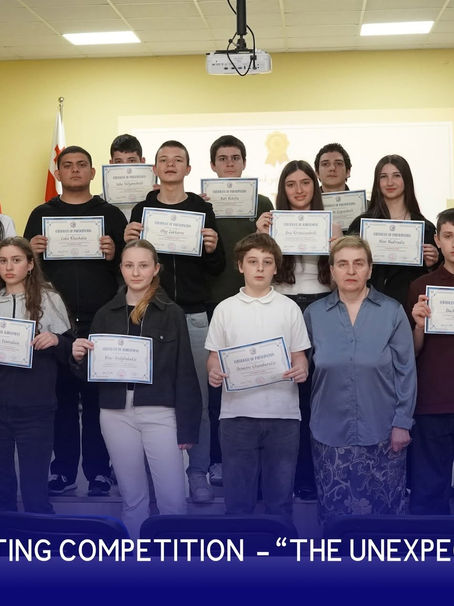 Grade 9 students of Georgian-American High School of Vake (GAHSV) and teacher Nato Mikava pose with certificates during the Creative Writing competition awards ceremony, “The Unexpected Twist.” The group stands in the school's conference hall with the Georgian, U.S., and school flags displayed in the background.
