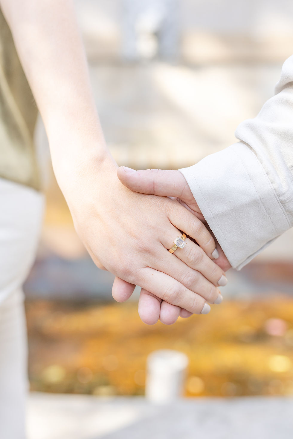 Two hands gently holding, one with a gold ring. Sunlight creates a warm glow in the blurred background, conveying a sense of intimacy.