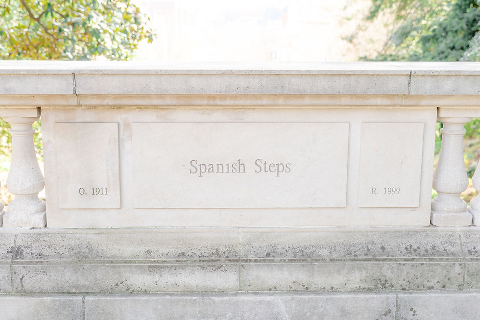 Stone balustrade with "Spanish Steps" engraved, dated 1911 and 1999. Sunlit greenery visible in the background, evoking tranquility.
