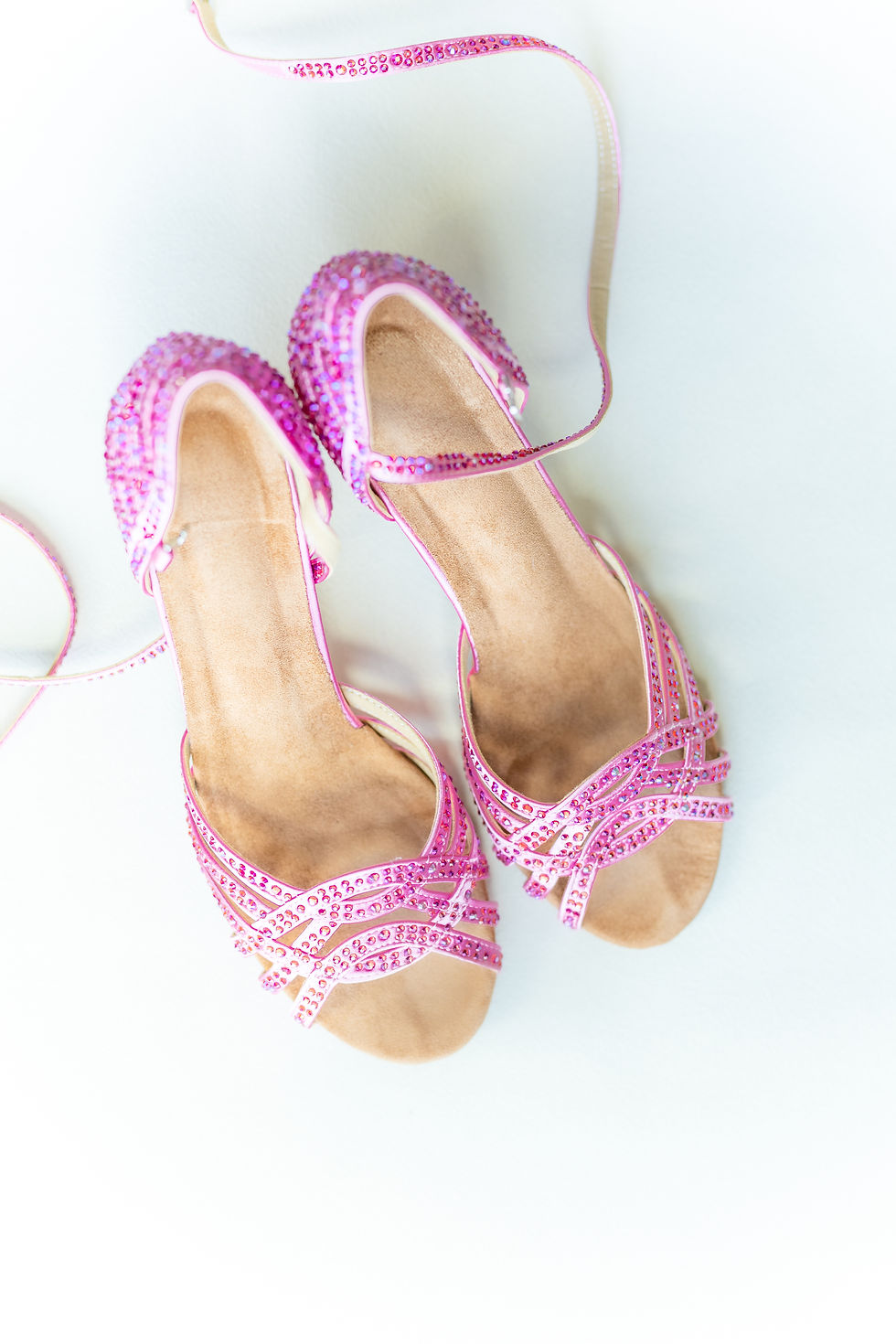 Pink sequined sandals with crisscross straps and ankle ties on a white background. Bright and sparkly, creating a festive mood.