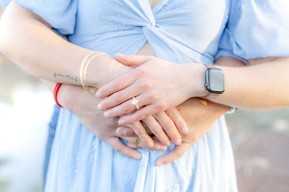 Hands embracing from behind, wearing a blue dress, gold bracelet, watch, and a ring. The mood is intimate and serene in soft lighting.