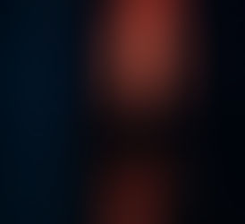 Man looking up at the penthouse window where a mysterious woman stands behind sheer curtains in a softly lit apartment building at night.