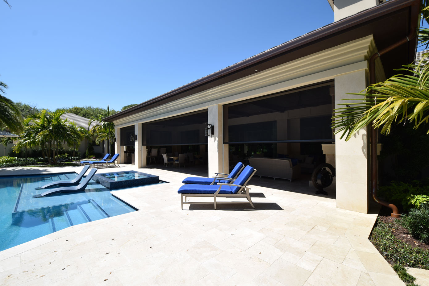 Bright sun shines on a swimming pool and nearby patio, which is partially covered by Fenetex retractable screens