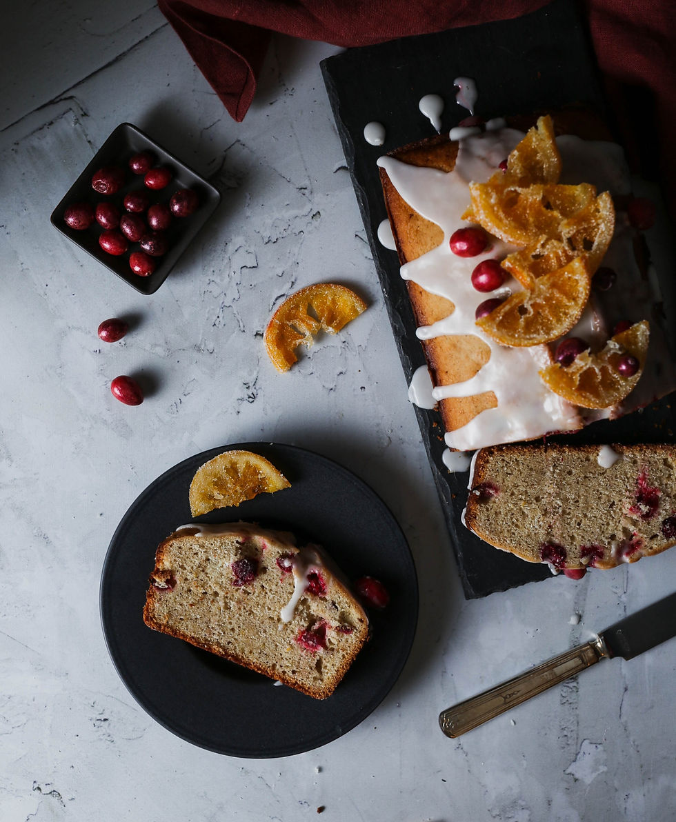 A slice of pound cake on a dark plate, with a side of candied orange and fresh cranberries.
