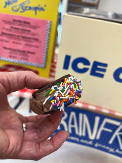 A hand holding a small ice cream sandwich with the brainfreeze checkered tablecloth and scooping box in the background