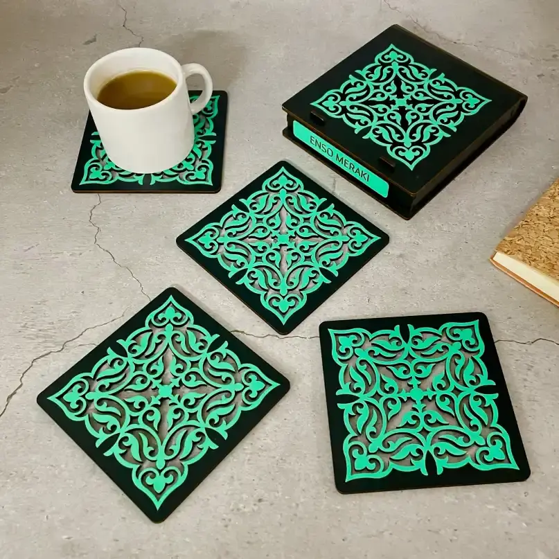 Tarini laser cut coaster set in black & teal with designer box and tea cup on grey backdrop, angled lifestyle image