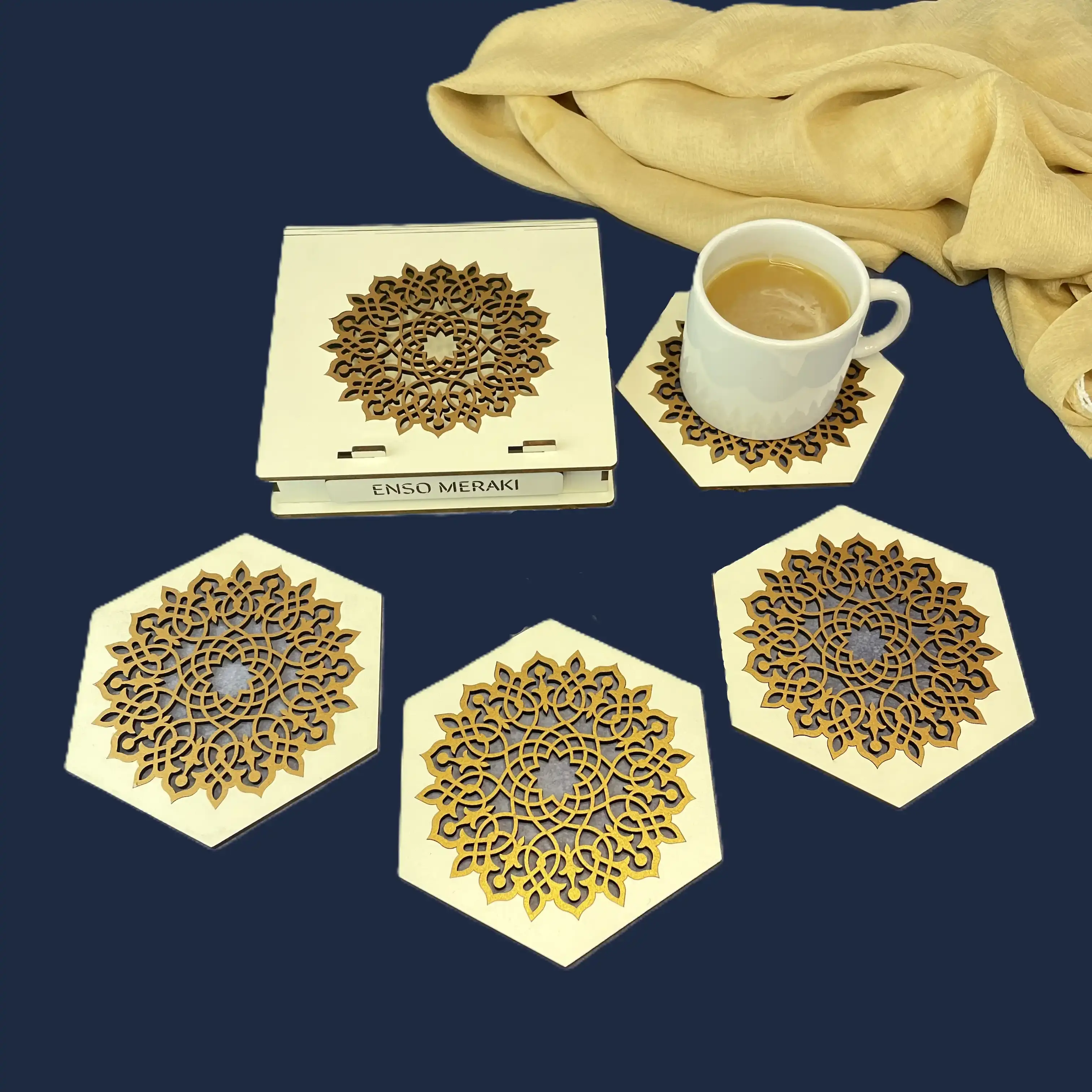 Aurelia laser cut coaster set and designer box in white and gold on dark blue background with tea cup, angled lifestyle shot